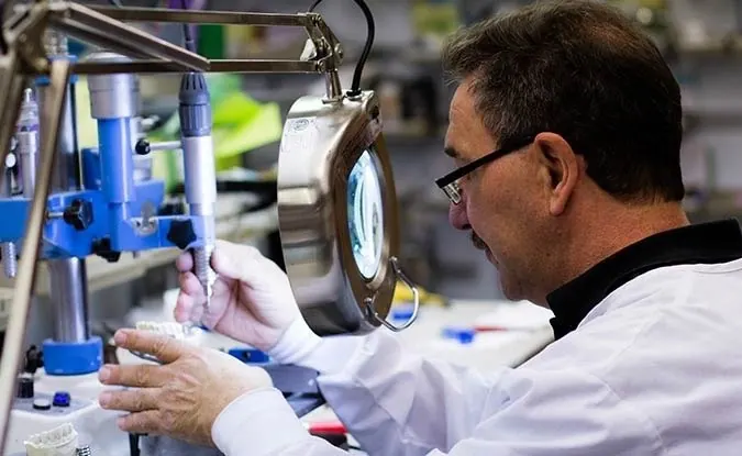 A technician in the practice's in-house laboratory working under a lighted magnifier.